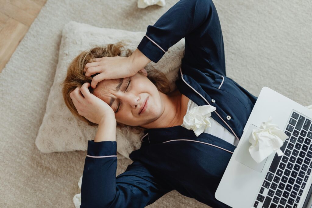 Beyond Burnout: How Wellness Coaching Helps High-Achievers Reclaim Their Energy Overhead view of a frustrated woman in loungewear with a laptop and crumpled papers, facing remote work stress.