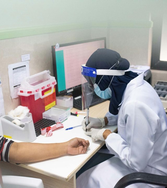Healthcare worker wearing PPE draws blood from a patient in a clinical setting.
